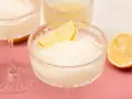Erfrischendes Limoncello Sorbet in einem Kristallglas, garniert mit einer Zitronenspalte. Ein halbe Zitrone liegt daneben.
