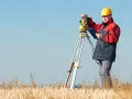 Geodeta w żółtym kasku pracuje z tachimetrem na polu. Zastanawiasz się, ile kosztuje geodeta?