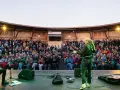 Konzert auf dem Tempelhofer Feld: Eine Musikerin spielt Gitarre vor einem begeisterten Publikum in einem hölzernen Amphitheater. Ein wahrer luftschloss tempelhofer feld Traum.