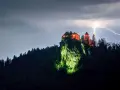 Zamek Poenari, oświetlony na czerwono, góruje nad skalistym zboczem podczas burzy z piorunami.