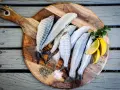 Plusieurs poissons frais sur une planche à découper en bois avec du sel, du poivre et des quartiers de citron.