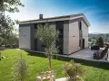 Esterno di case moderne con facciata in pannelli chiari e scuri, giardino curato e vista panoramica.