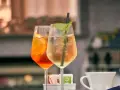 Dwa drinki w kieliszkach: pomarańczowy Aperol i jasny, z miętą. Aperol kontra Campari – wybór należy do Ciebie!