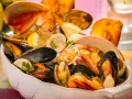 Un fumetto di pesce ricco di cozze, vongole e crostacei, guarnito con limone e prezzemolo, servito in una ciotola bianca.