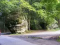 Fioletowy samochód pokonuje zakręty na leśnej drodze. Trasa 100 zakrętów wita podróżnych skalnymi formacjami.