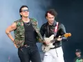 Albert Hammond Jr. w kamizelce moro i okularach stoi obok gitarzysty w skórzanej kurtce, grającego na białej gitarze.