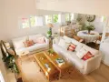 Salón luminoso con sofás blancos, mesas de mimbre y un rincón de comedor. La distribución de salones irregulares crea un espacio acogedor y funcional.