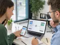 Zwei Personen besprechen am Laptop und Smartphone ein Webdesign. Die Bildschirme zeigen eine Verknüpfung, die an amp google erinnert.
