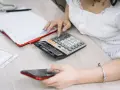 Kobieta liczy na kalkulatorze, przygotowując się do rozliczenia podatkowego w Holandii. Obok leży telefon i notatnik.
