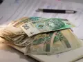 Stos banknotów 100 zł na dokumentach. Czy to wystarczy na najniższą emeryturę?