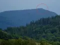 Górzyste krajobrazy czeskich Izery, z zalesionymi zboczami i skalistym szczytem zaznaczonym czerwoną obwódką.