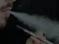 Un hombre con barba exhala vapor de un vapeador, similar al estilo Heisenberg.