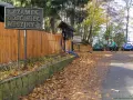 Tablica z napisem "Zamek GOSCINIEC MISYJNY" przy drewnianym płocie. Jesienny parking z samochodami i opadłymi liśćmi.