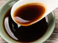 Łyżka z ciemnym, błyszczącym płynem, idealnym jako ocet balsamiczny do mięsa.