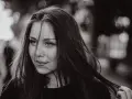 Portret młodej kobiety z burzą ciemnych włosów. Jej spojrzenie jest lekko zadumane, a usta subtelnie uśmiechnięte. Grzywka dodaje jej tajemniczości.