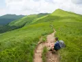 Turysta odpoczywa na szlaku, podziwiając zielone połoniny. Gdzie w Bieszczady? Tu, gdzie ścieżka wije się wśród traw, a szczyty kuszą.