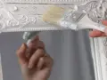 Pintura a la tiza blanco antiguo en un marco de espejo ornamentado. Una mano aplica la pintura con una brocha, creando un acabado desgastado.