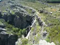 Cascada cayendo por rocas escarpadas cerca de un pico ocejon, rodeado de vegetación verde y rocas.
