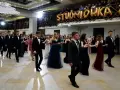 Młodzi ludzie w eleganckich strojach, tańczący poloneza na balu studniówkowym.