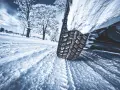 La gomma ghiaccio affronta la neve su una strada invernale, lasciando profonde tracce. Alberi innevati sullo sfondo.