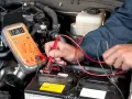 A person uses a multimeter to test a car battery in an engine bay.