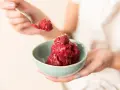 Ein Löffel Himbeersorbet-Rezept wird über eine Schüssel mit dem leuchtend roten Dessert gehalten, garniert mit einer Himbeere.