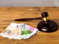 Ein Richterhammer liegt neben Euro-Scheinen. Die Frage "wie lange muss eine Rechtsschutzversicherung bestehen?" wird hier visuell thematisiert.