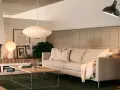 En ljus soffa med kuddar och en filt, framför ett soffbord i trä. En golvlampa och en taklampa lyser upp rummet. Perfekt för att mäta soffa mått.