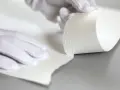 Manos enguantadas manipulan papel texturizado, mostrando su grosor. Esto ayuda a entender qué es el gramaje.