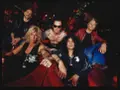 Cinq musiciens, un groupe de slash, posent sur un canapé rouge. Ils portent des vestes en cuir et des bijoux.