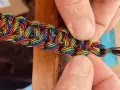 Mani che creano nodi per braccialetti elastici color arcobaleno, un'arte che unisce creatività e praticità.
