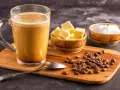 Ein Glas Bulletproof Coffee mit Butterwürfeln, Kokosöl und Kaffeebohnen auf einem Holzbrett.