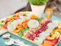 Eine bunte Antipasti Platte anrichten mit Burrata, Kirschen, Pfirsichen, Tomaten und Prosciutto.