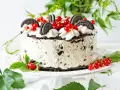 Pyszny tort z kawałkami oreo ciastka, udekorowany bitą śmietaną i czerwonymi porzeczkami.