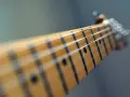 Zbliżenie na gryf gitary, gdzie ja gram na gitarze chwyty. Widać struny i progi.