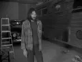 Neil Young, jung und nachdenklich, steht vor einem umgebauten Bus. Eine Leiter und ein Oldtimer im Hintergrund.