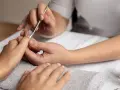 Profesjonalny manicure kombinowany w toku. Dłonie są zadbane, a kosmetyczka precyzyjnie pracuje narzędziami.