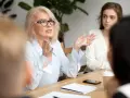 Kobieta w okularach, omawiająca ocenę pracy nauczyciela, gestykuluje do grupy.