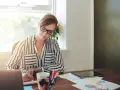 Mujer con gafas trabaja en su escritorio, revisando documentos y gráficos. Quizás está lidiando con gastos de difícil justificación.