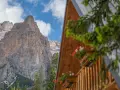 Drewniany domek z kwiatami w skrzynkach na tle skalistych Dolomitów.