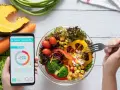 Aplikacja pokazuje 1200 kcal, podczas gdy ręka sięga widelcem po świeżą sałatkę.