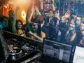 Feiernde Menschen tanzen im Club, während ein DJ auflegt. Eine druckbare muttizettel vorlage zum ausdrucken wäre hier perfekt für die nächste Party!