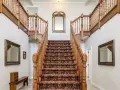 Elegante escalera antigua con alfombra de estilo persa y barandillas de madera. Un espejo dorado decora la pared central, complementando el revestir escalera antigua.