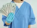 Higienistka stomatologiczna w niebieskim fartuchu pokazuje wachlarz banknotów 20 dolarowych. Zastanawiasz się, ile zarabia higienistka stomatologiczna?