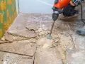 Skuwanie płytek młotem udarowym. Rozpoczyna się remont łazienki, widać porozbijane płytki i kurz.