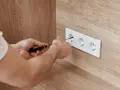 Ręce majsterkowicza przykręcają gniazdko. Dbałość o detale zapewnia bezpieczne napięcie skuteczne w domu.