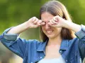 Ragazza con espressione infastidita, si stropiccia gli occhi con le mani, forse per il sole o per la stanchezza.