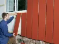 Man monterar en röd lockpanel vid ett fönster.