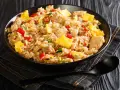 Un plato humeante de arroz chaufa con trozos de pollo, huevo revuelto, pimientos rojos y cebolla verde.