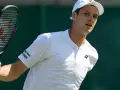Hubert Hurkacz w białej koszulce i czapce, gotowy do uderzenia rakietą na Wimbledonie.